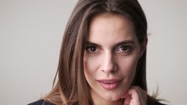 Güzel, baştan çıkarıcı bir kadının yakın çekim görüntüsü stüdyoda beyaz arka planda tek başına kameraya poz veriyor.