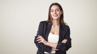 Gündelik kıyafetler giyen mutlu genç bir kadın gülümsüyor. Kollarını katlayarak stüdyoda beyaz arka planda soyutlanmış bir şekilde duruyor.