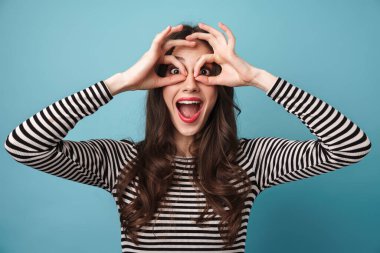 Mavi arka planda izole edilmiş parmaklarıyla gülüp eğlenen eğlenceli genç bir kadın görüntüsü
