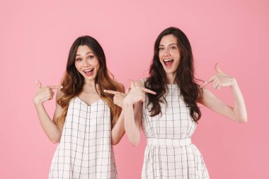 Gülümseyen ve kendini gösteren neşeli kadınların resmi pembe arka planda izole edilmiş.