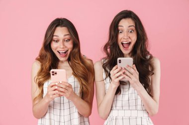 Şaşırdıklarını ifade eden ve pembe arka planda izole edilmiş cep telefonları kullanan heyecanlı beyaz kadın görüntüsü