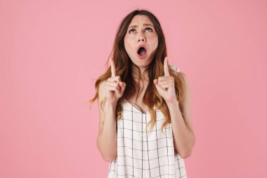 Hoşnutsuz, hoş bir kadının pembe arka planda yalnız bir şekilde şaşkınlığını göstermesi ve parmaklarını yukarı kaldırması.