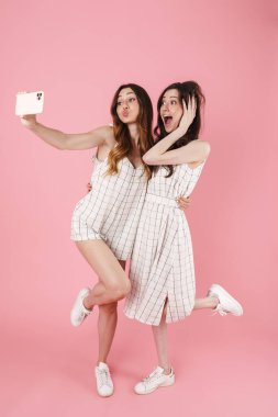 Pembe arka planda izole edilmiş cep telefonundan selfie çekerken öpüşen mutlu kadınların görüntüsü
