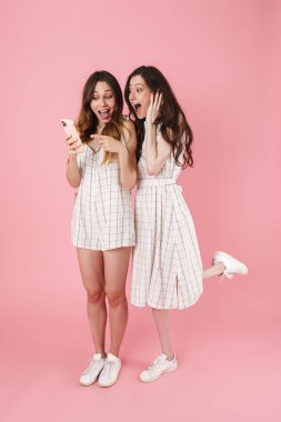 Pembe arka planda izole edilmiş cep telefonunu kullanan ve işaret eden mutlu çekici kadınların görüntüsü