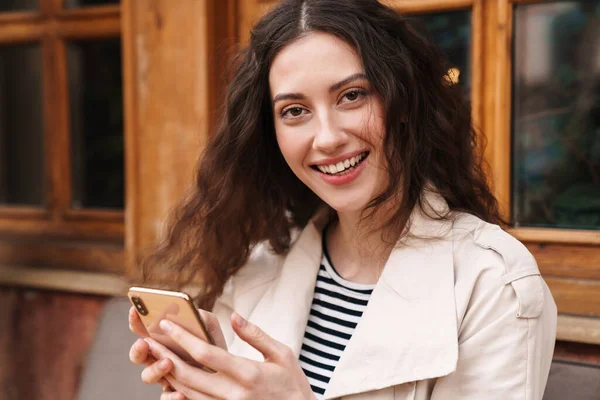 Obrázek Šťastné Brunetky Žena Pomocí Mobilního Telefonu Úsměvem Při Posezení — Stock fotografie