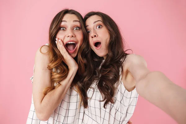 Image of excited pretty women expressing surprise while taking selfie photo isolated over pink background