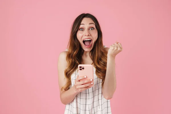 携帯電話を使用して興奮したかわいい女性のイメージとピンクの背景に隔離された勝者のジェスチャーを作る — ストック写真