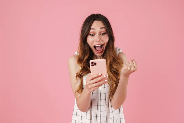 携帯電話を使用して興奮したかわいい女性のイメージとピンクの背景に隔離された勝者のジェスチャーを作る — ストック写真
