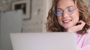 Gözlük takan genç, sarışın bir kadın laptopuyla içeride, masada oturuyor.