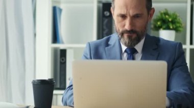 Odaklanmış olgun bir adam ofiste dizüstü bilgisayarıyla çalışıyor.