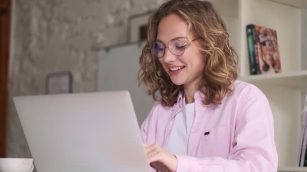 Memnun Gözlüklü Genç Sarışın Bir Kadın Laptopunda Içeride Masada Oturuyor — Stok video