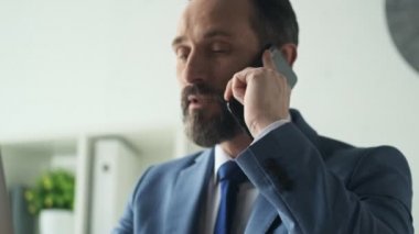 Ciddi, olgun bir adam ofiste çalışırken telefonla konuşuyor.