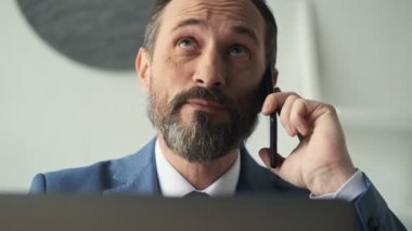Yakışıklı, olgun bir adam ofiste çalışırken telefonla konuşuyor.