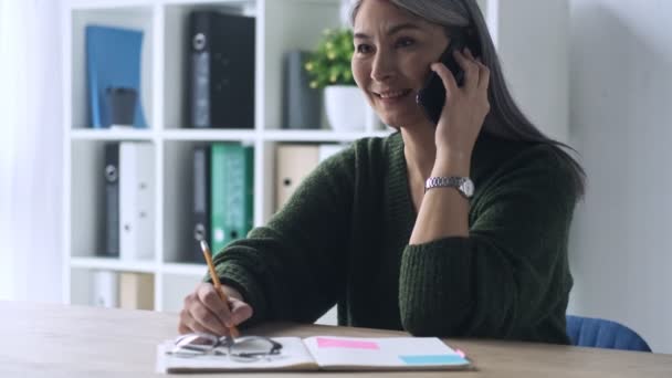 Uma Empresária Madura Feliz Está Fazendo Anotações Enquanto Fala Smartphone — Vídeo de Stock