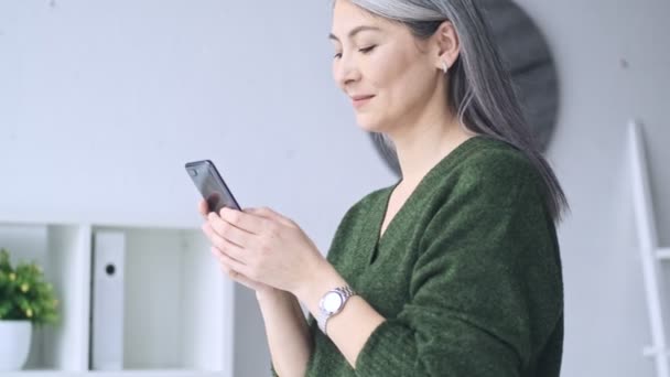 一位长白发的漂亮的成熟女商人在办公室工作时正在用她的智能手机 — 图库视频影像