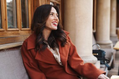 Açık hava kafeteryasında oturmuş gülen mutlu bir yetişkin kadın resmi.