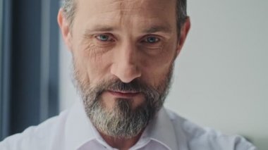 Kendine güvenen olgun bir adam ofiste dikilirken kameraya bakıyor.