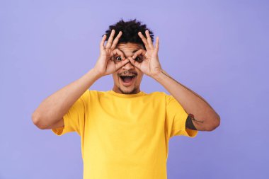 Mutlu Afro-Amerikalı adamın fotoğrafı. Tamam işareti gösteriyor ve sürpriz yapıyor. Mor arka planda izole edilmiş.