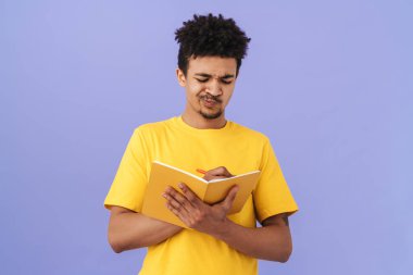 Afro-Amerikalı adamın suratını buruşturduğu ve not aldığı bir fotoğraf. Mor arka planda izole edilmiş.