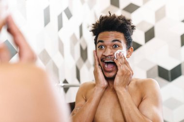 Yarı çıplak, Afro-Amerikan bir adamın yüzünü temizlediği ve banyoda aynaya baktığı fotoğraf.