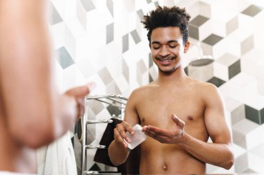 Yarı çıplak Afrikalı Amerikalı bir adamın tıraş losyonu sürerken ve banyoda aynaya bakarken çekilmiş fotoğrafı.