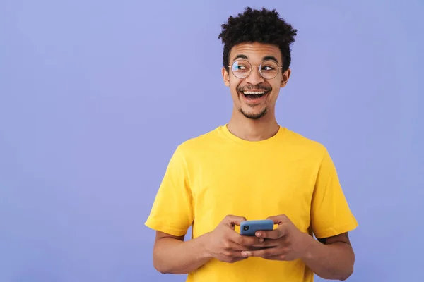 照片上的兴奋的非洲裔美国人 戴着眼镜 面带微笑 用智能手机与紫色背景隔离 — 图库照片