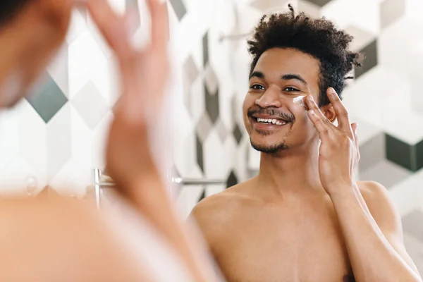 幸せの半分裸アフリカ系アメリカ人男性の写真顔クリームを適用し バスルームでミラーを見て — ストック写真