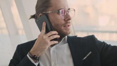 Yakışıklı, genç, sakallı bir iş adamı şehir merkezindeki bir kafede çalışırken akıllı telefonuyla konuşuyor.
