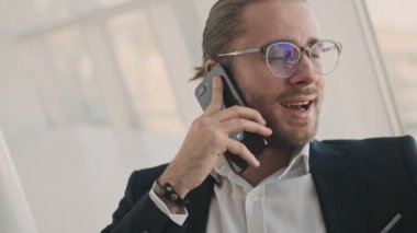 Çekici, genç, sakallı bir iş adamı kapalı bir kafede çalışırken akıllı telefonuyla konuşuyor.