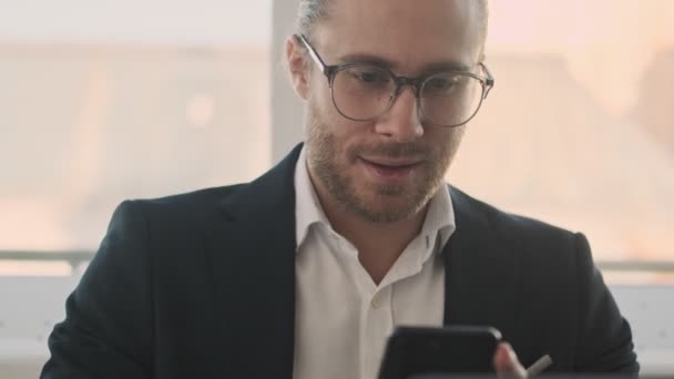 Egy Vonzó Fiatal Szakállas Üzletember Használja Okostelefonját Miközben Egy Laptopon — Stock videók