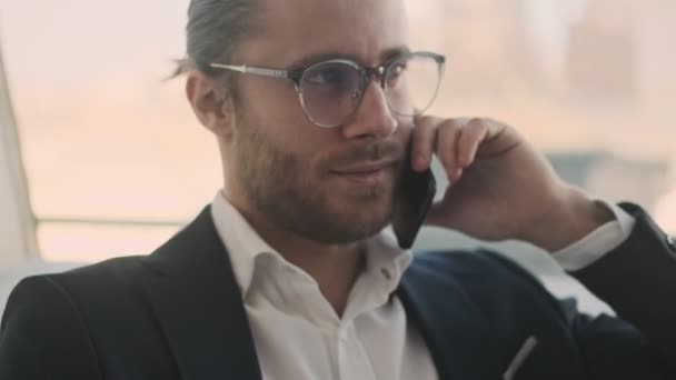 一位年轻英俊的大胡子商人在室内一家城市咖啡店里拿着纸质文件 一边用智能手机聊天 — 图库视频影像