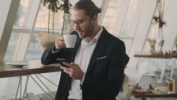 Soustředěný Pohledný Mladý Vousatý Podnikatel Používá Svůj Smartphone Zatímco Pije — Stock video