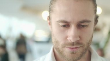 Sakin genç bir iş adamının yakın çekim görüntüsü şehir merkezindeki bir kafede kameraya bakıyor.