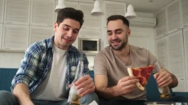 Mutlu, gülümseyen duygusal adamlar evde oturma odasında oturmuş abur cubur yerken, pizza yerken ve bira içerken selfie çekiyorlar.