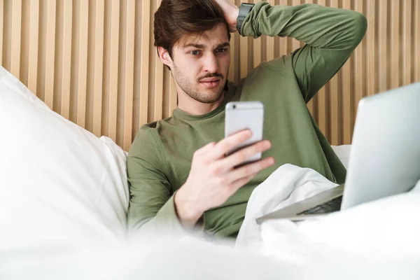 Foto Homem Caucasiano Confuso Com Bigode Usando Celular Laptop Enquanto — Fotografia de Stock