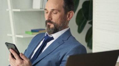 Kendinden emin, olgun bir adam ofiste oturan bu akıllı telefona bakıyor.