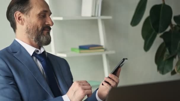 Ein Erfolgreicher Lächelnder Älterer Mann Sitzt Mit Seinem Smartphone Büro — Stockvideo