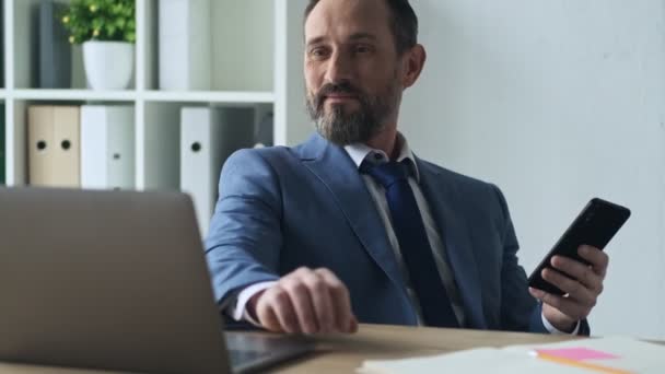 在办公室工作时 一个自信的 面带微笑的成熟男人正在用他的智能手机 — 图库视频影像