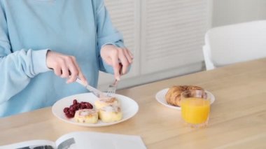 Genç bir kadının kırpılmış görüntüsü peynirli krep yiyor. Sabahları beyaz mutfakta oturuyor.