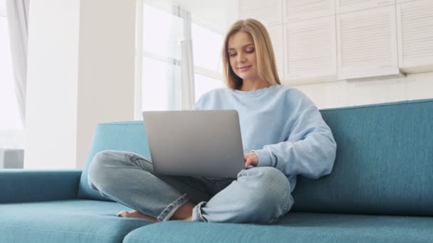 Šťastná Mladá Blondýna Používá Svůj Stříbrný Notebook Sedí Pohovce Obývacím — Stock video