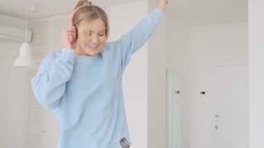 Mutlu, genç, sarışın bir kadın evdeki oturma odasında kulaklıkla müzik dinlemekten zevk alıyor.
