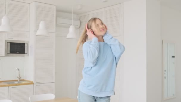一位面带微笑的金发年轻女子正享受着在家里客厅里用耳机听音乐的乐趣 — 图库视频影像
