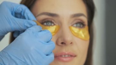 Profesyonel bir doktor-kozmetikçinin yakın plan görüntüsü güzellik salonundaki kadın müşterilere altın bantlar takıyor.