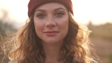 Şapkalı, ekose gömlekli, gülümseyen sarışın bir kadının dışarıda poz verip kameraya baktığı yakın görüntü.