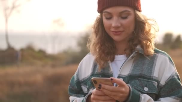 Usmívající Blondýna Žena Nosí Klobouk Kostkované Tričko Pomocí Smartphone Venku — Stock video