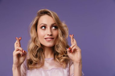 Morarmış arka planda parmaklarını çapraz yapıp gülümseyen güzel, heyecanlı bir kadın görüntüsü.