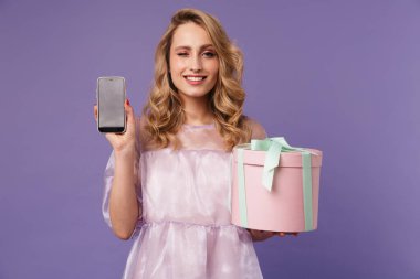 Mor arka planda izole edilmiş cep telefonu ve hediye kutusunu gösteren heyecanlı genç bir kadının görüntüsü
