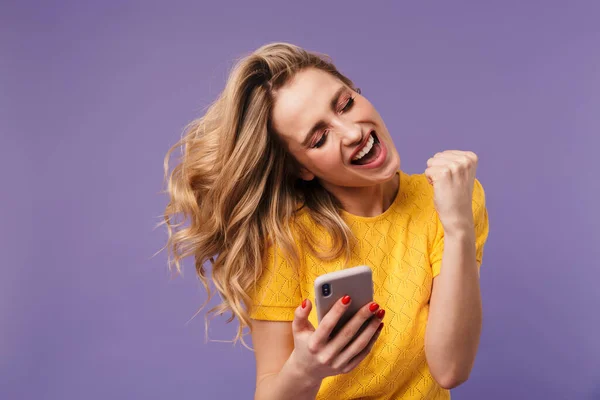 照片上兴奋的漂亮女人拿着手机在紫色背景下做得奖手势 — 图库照片
