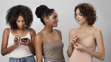 Üç mutlu çok ırklı kadın, beyaz arka plan üzerinden birbirleriyle iletişim kurarken akıllı telefondan resmi izliyor.