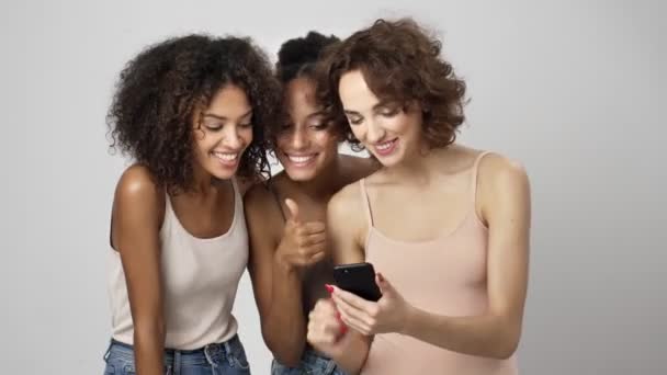 3人の笑顔の多民族の女性が白い背景に隔離されたスマートフォンを使用してビデオ接続と話しています — ストック動画